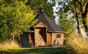 A sunny picture of a hexagonal scandanavian BBQ hut set amongst the plum and apple trees in the orchard.