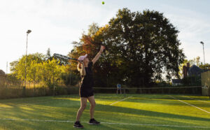All weather tennis court at Orchard Escapes set amongst trees and surrounding countryside, players enjoying a game outdoors.
